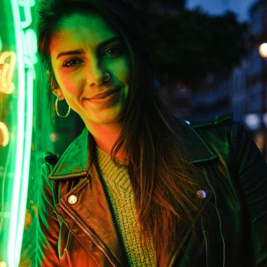 Frau vor Neonlicht Eine dunkelhaarige Frau lehnt an einem grünen Neonschild und lächelt.