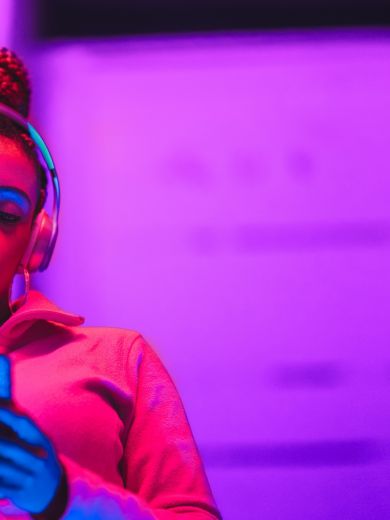 Frau mit Smartphone Eine Frau steht im pinken Licht mit Kopfhörern auf und schaut auf ihr Handy