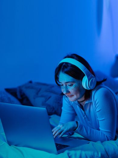 Frau auf dem Bett mit Laptop Eine Frau mit Kopfhörern liegt auf einem Bett mit einem Laptop.