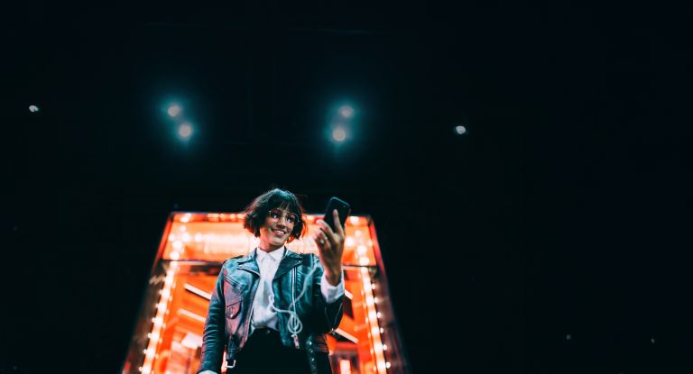 Frau mit Handy in der Hand Eine Frau steht mit einem Handy in der Hand vor einem Neongebäude