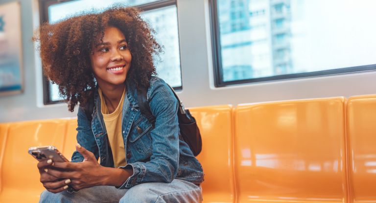 Junge Frau im Zug Eine junge, glückliche Frau die in einem leeren Zug sitzt und ein Smartphone in der Hand hält.