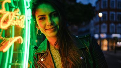 Frau vor Neonlicht Eine dunkelhaarige Frau lehnt an einem grünen Neonschild und lächelt.