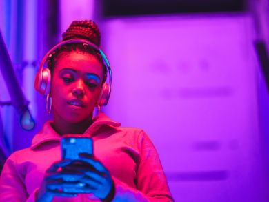 Frau mit Smartphone Eine Frau steht im pinken Licht mit Kopfhörern auf und schaut auf ihr Handy