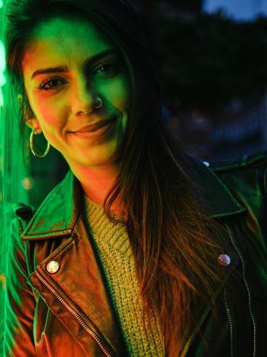 Frau vor Neonlicht Eine dunkelhaarige Frau lehnt an einem grünen Neonschild und lächelt.