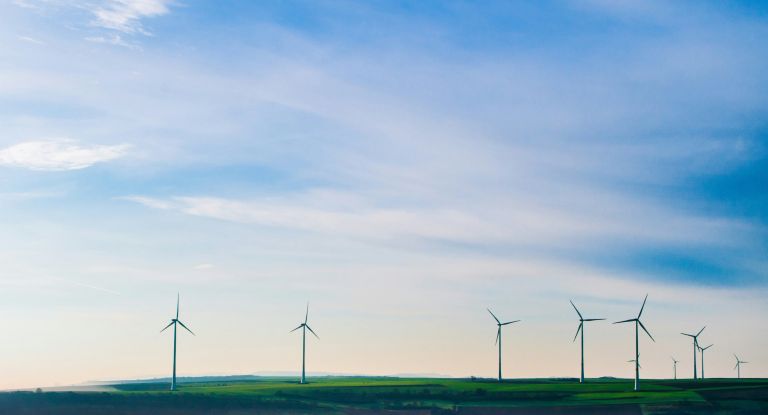Windkraftwerke Mehrere Windkraftwerke erzeugen Strom auf einer Wiese vor einem blauen und leicht wolkigem Himmel