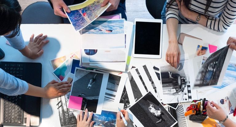 Tisch mit Arbeitsmaterial Auf einem Tisch liegen viele Blätter, ein Tablet und ein Laptop. Mehrere Hände sehen beschäftigt aus.